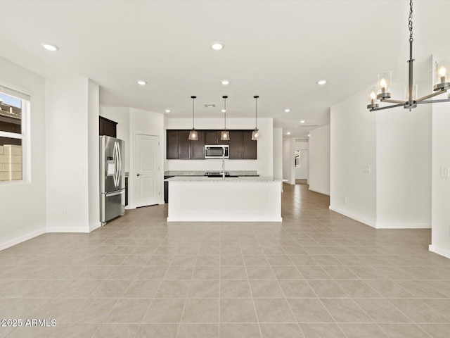 kitchen with light stone counters, stainless steel appliances, hanging light fixtures, open floor plan, and a kitchen island with sink