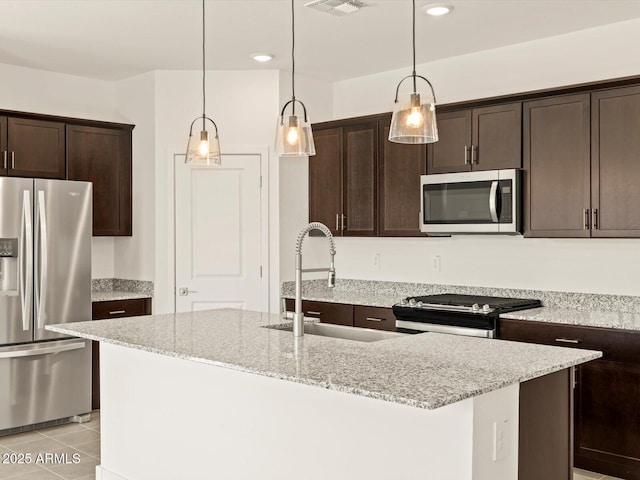 kitchen with stainless steel appliances, light stone counters, a sink, and a center island with sink