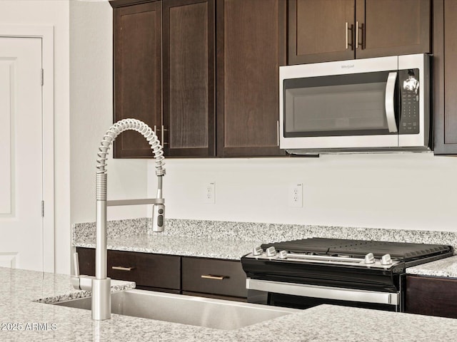 kitchen featuring stainless steel appliances, light stone counters, a sink, and dark brown cabinets