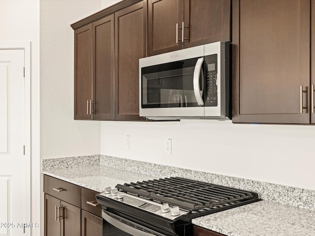 kitchen featuring stainless steel appliances, dark brown cabinetry, and light stone counters