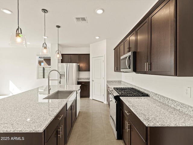 kitchen with stainless steel appliances, a kitchen island with sink, a sink, and hanging light fixtures