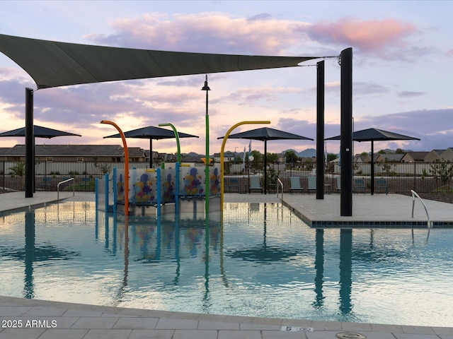 pool at dusk featuring a water play area and fence