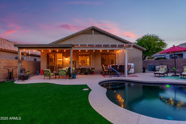 rear view of property featuring fence, a patio, stucco siding, a fenced in pool, and a yard