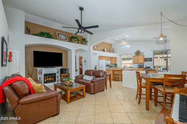 living area featuring a ceiling fan, arched walkways, high vaulted ceiling, a glass covered fireplace, and light tile patterned flooring