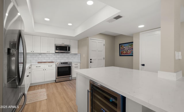 7424 N Via Camello Del Norte Unit 185, Scottsdale, AZ 85258 - kitchen with stainless steel appliances, wine cooler, light stone countertops, white cabinetry, and light wood finished floors