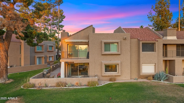 7424 N Via Camello Del Norte Unit 185, Scottsdale, AZ 85258 - back of property at dusk with a balcony, stucco siding, a lawn, and a chimney