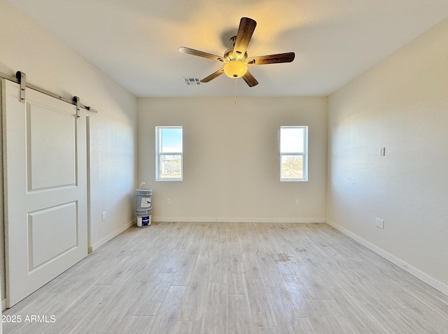 unfurnished room featuring a barn door, plenty of natural light, wood finished floors, and visible vents