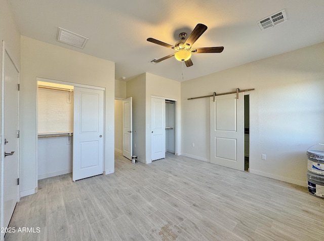 unfurnished bedroom featuring visible vents, light wood finished floors, baseboards, multiple closets, and a barn door