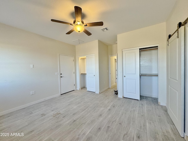 unfurnished bedroom with visible vents, two closets, baseboards, a barn door, and light wood-style flooring