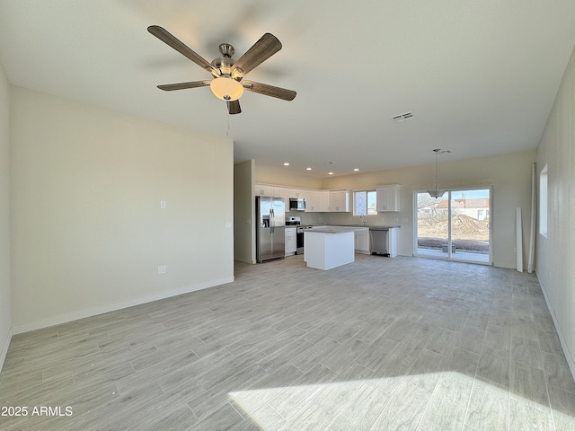 unfurnished living room featuring visible vents, a sink, light wood finished floors, baseboards, and ceiling fan