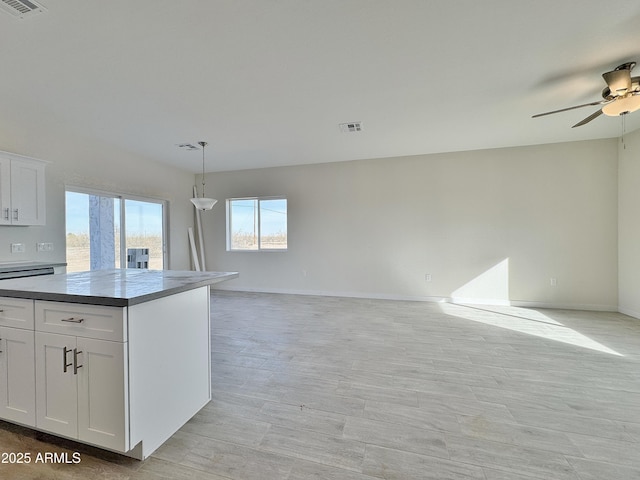 kitchen with open floor plan, white cabinets, visible vents, and ceiling fan