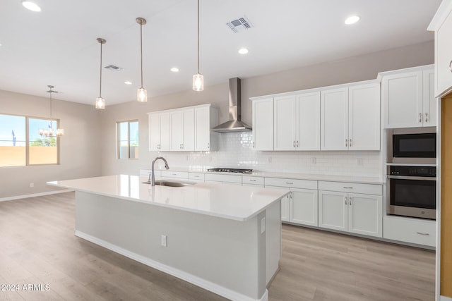 kitchen with wall chimney range hood, appliances with stainless steel finishes, hanging light fixtures, sink, and white cabinets