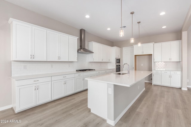 kitchen featuring white cabinets, light hardwood / wood-style floors, wall chimney range hood, and a center island with sink