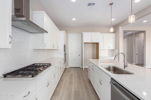 kitchen featuring stainless steel appliances, sink, light wood-type flooring, wall chimney range hood, and pendant lighting