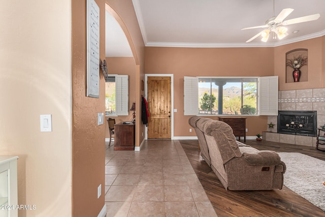 living room with a tiled fireplace, ceiling fan, tile patterned flooring, and ornamental molding