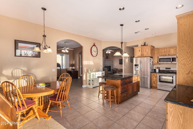 kitchen featuring ceiling fan with notable chandelier, appliances with stainless steel finishes, decorative light fixtures, a kitchen island, and a kitchen bar