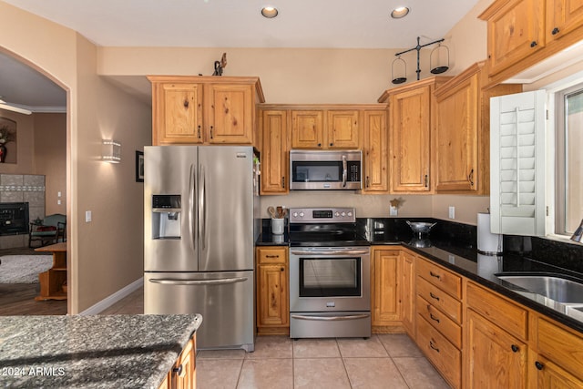 kitchen featuring dark stone counters, sink, light tile patterned floors, and stainless steel appliances