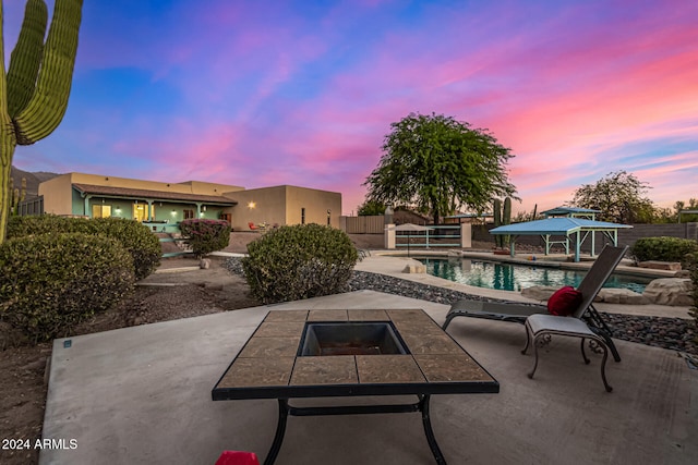 patio terrace at dusk featuring a gazebo, a fenced in pool, and an outdoor fire pit