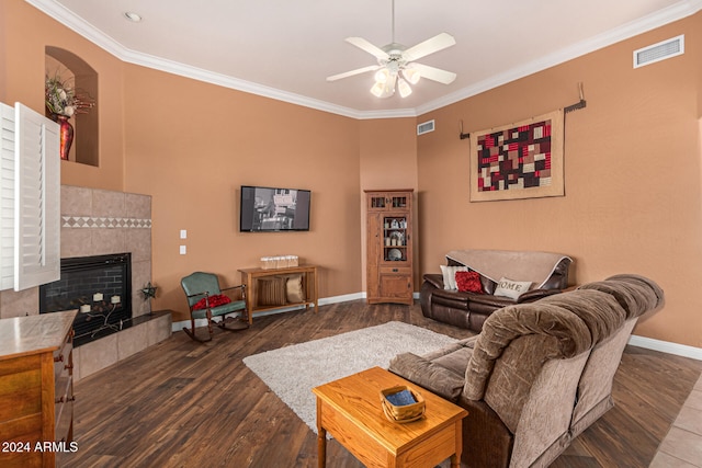 living room featuring dark hardwood / wood-style floors, ceiling fan, crown molding, and a tiled fireplace