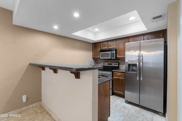 3235 E Camelback Rd Unit 124, Phoenix, AZ 85018 - kitchen featuring stainless steel appliances, a tray ceiling, a breakfast bar, backsplash, and a peninsula