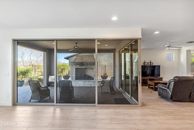 doorway with a stone fireplace, light hardwood / wood-style floors, and ceiling fan