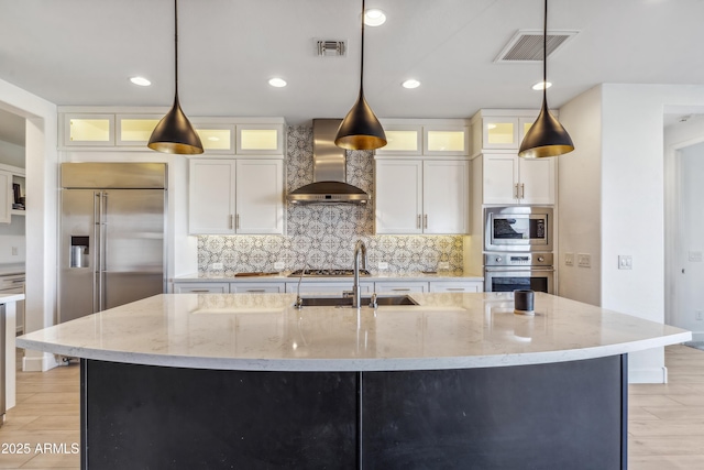 kitchen featuring pendant lighting, wall chimney exhaust hood, and a center island with sink