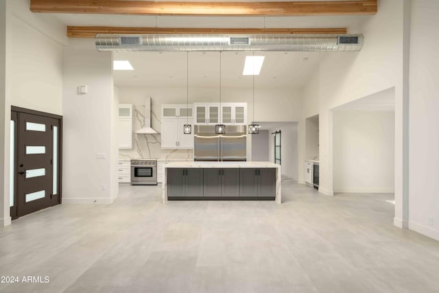 kitchen featuring white cabinetry, stainless steel appliances, a towering ceiling, and wall chimney range hood