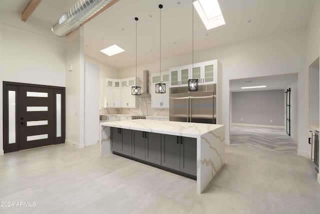 kitchen featuring a towering ceiling, a large island, pendant lighting, white cabinetry, and built in fridge