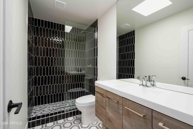 bathroom featuring tile patterned flooring, vanity, tiled shower, and toilet