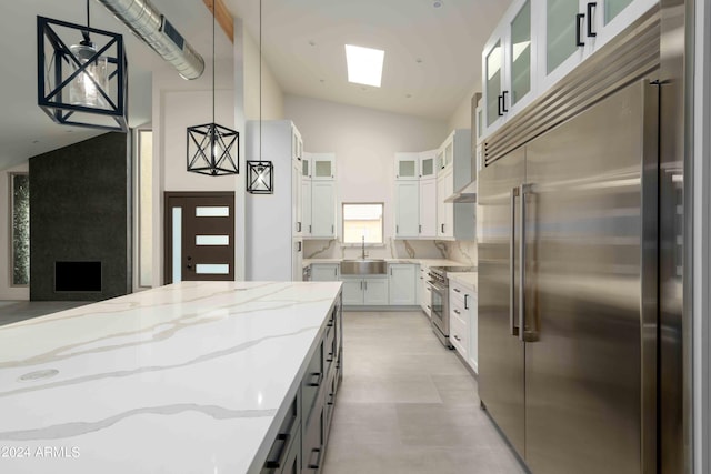 kitchen with light stone countertops, stainless steel appliances, sink, white cabinets, and hanging light fixtures