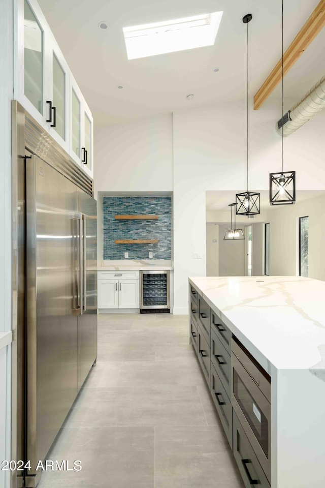 kitchen with wine cooler, built in appliances, decorative light fixtures, light stone counters, and white cabinetry