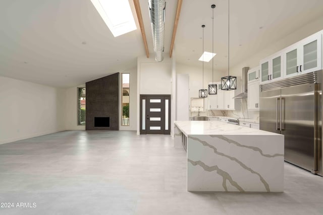 kitchen featuring white cabinetry, built in fridge, light stone counters, high vaulted ceiling, and decorative light fixtures