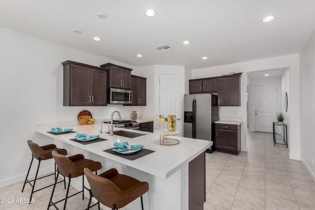 kitchen featuring sink, kitchen peninsula, a breakfast bar area, dark brown cabinets, and appliances with stainless steel finishes