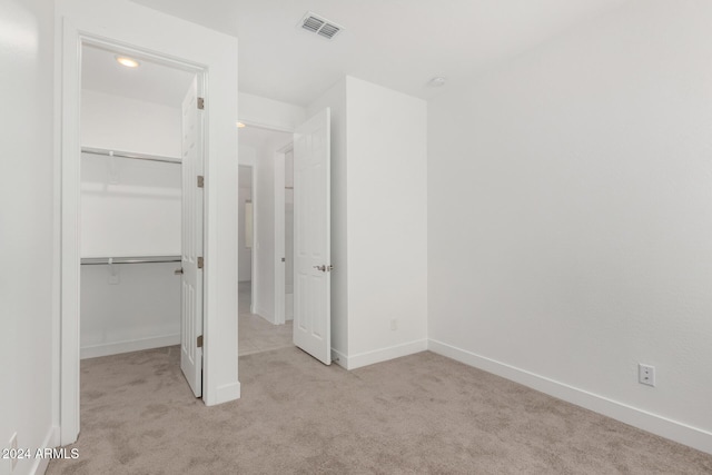 unfurnished bedroom featuring a walk in closet, light carpet, and a closet