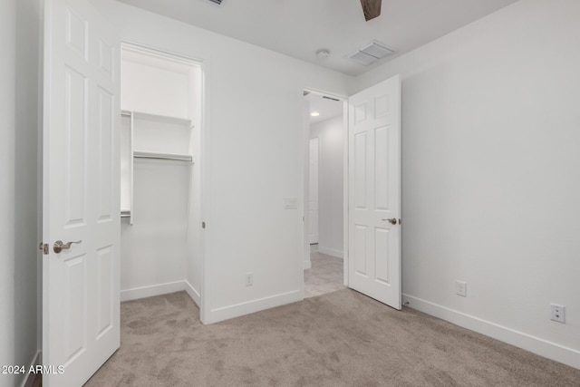 unfurnished bedroom with a walk in closet, light carpet, a closet, and ceiling fan