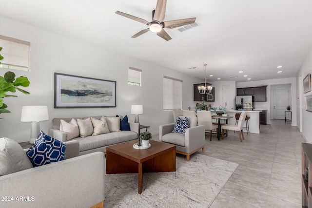 tiled living room with ceiling fan with notable chandelier