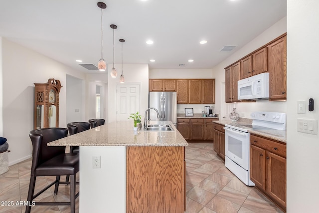 kitchen featuring a breakfast bar, pendant lighting, white appliances, and a kitchen island with sink