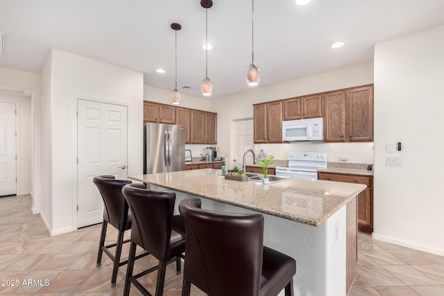 kitchen featuring light stone countertops, a breakfast bar, white appliances, decorative light fixtures, and an island with sink