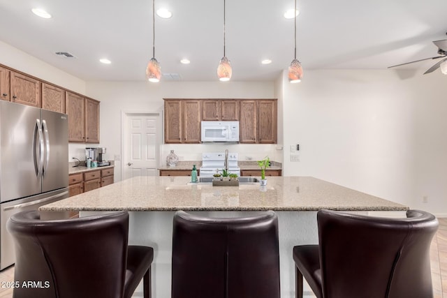 kitchen featuring pendant lighting, sink, white appliances, and an island with sink