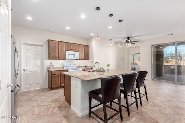 kitchen featuring white appliances, ceiling fan, sink, pendant lighting, and an island with sink