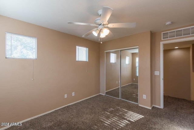 unfurnished bedroom with dark colored carpet, ceiling fan, and a closet