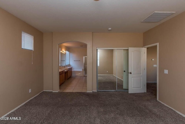 unfurnished bedroom featuring light carpet, sink, a closet, and ensuite bathroom