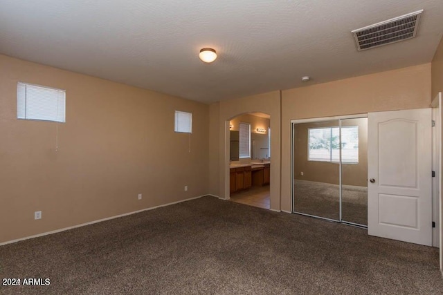 unfurnished bedroom with ensuite bathroom, carpet, a textured ceiling, and a closet