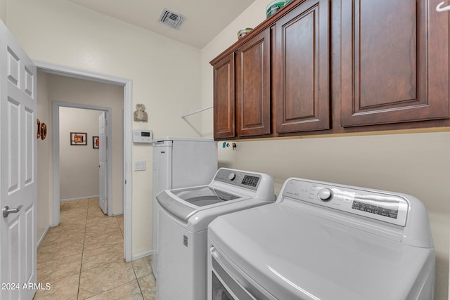 washroom featuring washing machine and clothes dryer, light tile patterned floors, and cabinets