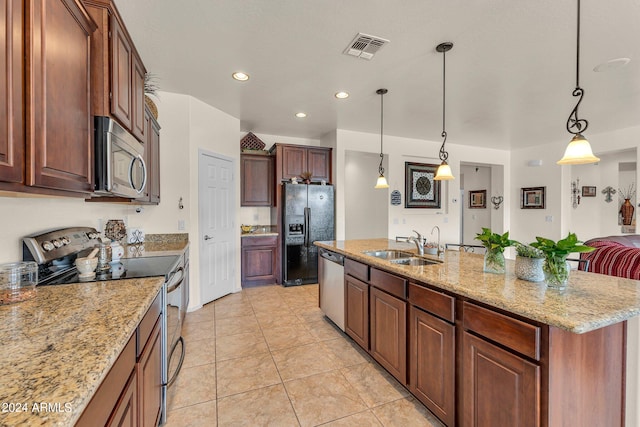 kitchen with light tile patterned flooring, a kitchen island with sink, decorative light fixtures, light stone counters, and appliances with stainless steel finishes