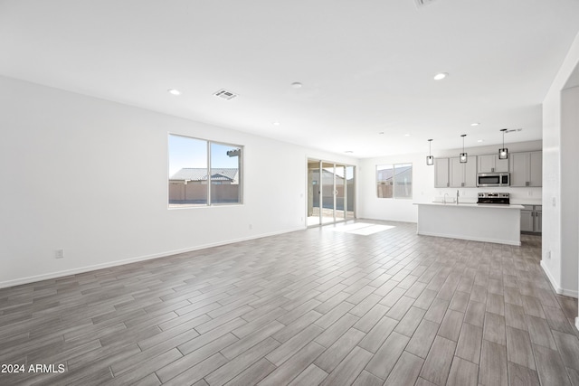 unfurnished living room featuring light wood-type flooring, a healthy amount of sunlight, visible vents, and recessed lighting