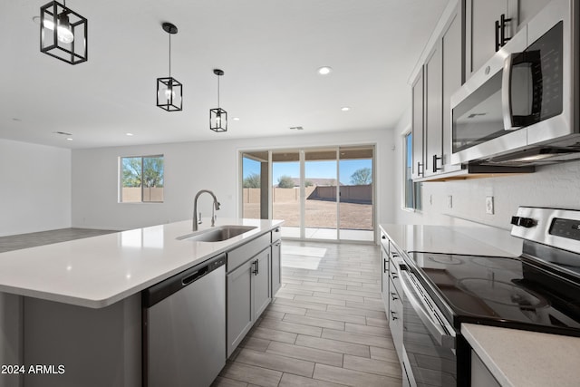 kitchen featuring pendant lighting, stainless steel appliances, light countertops, gray cabinetry, and a sink