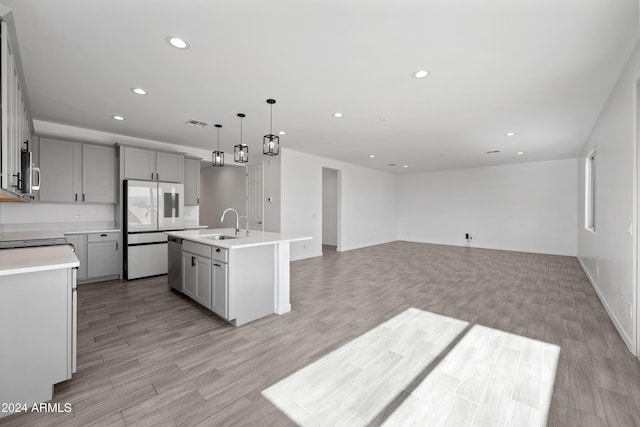 kitchen with light wood finished floors, stainless steel appliances, gray cabinets, light countertops, and a sink