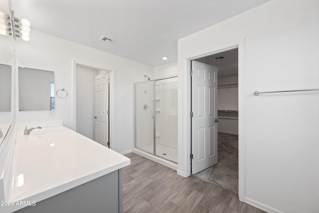 full bathroom with wood finished floors, visible vents, vanity, a shower stall, and a walk in closet