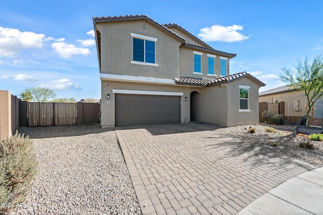 mediterranean / spanish house featuring decorative driveway, a tile roof, fence, and stucco siding